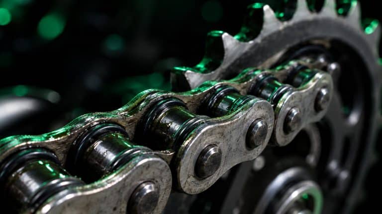 Primer plano de una cadena de moto con retenes O-ring lubricada sobre la corona